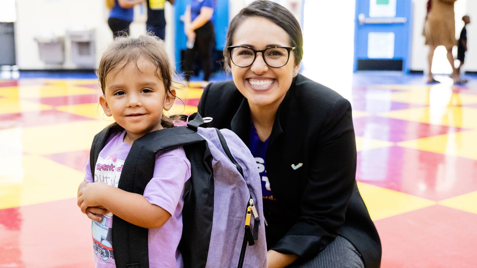 a woman sits next to a young child who has a backpack on